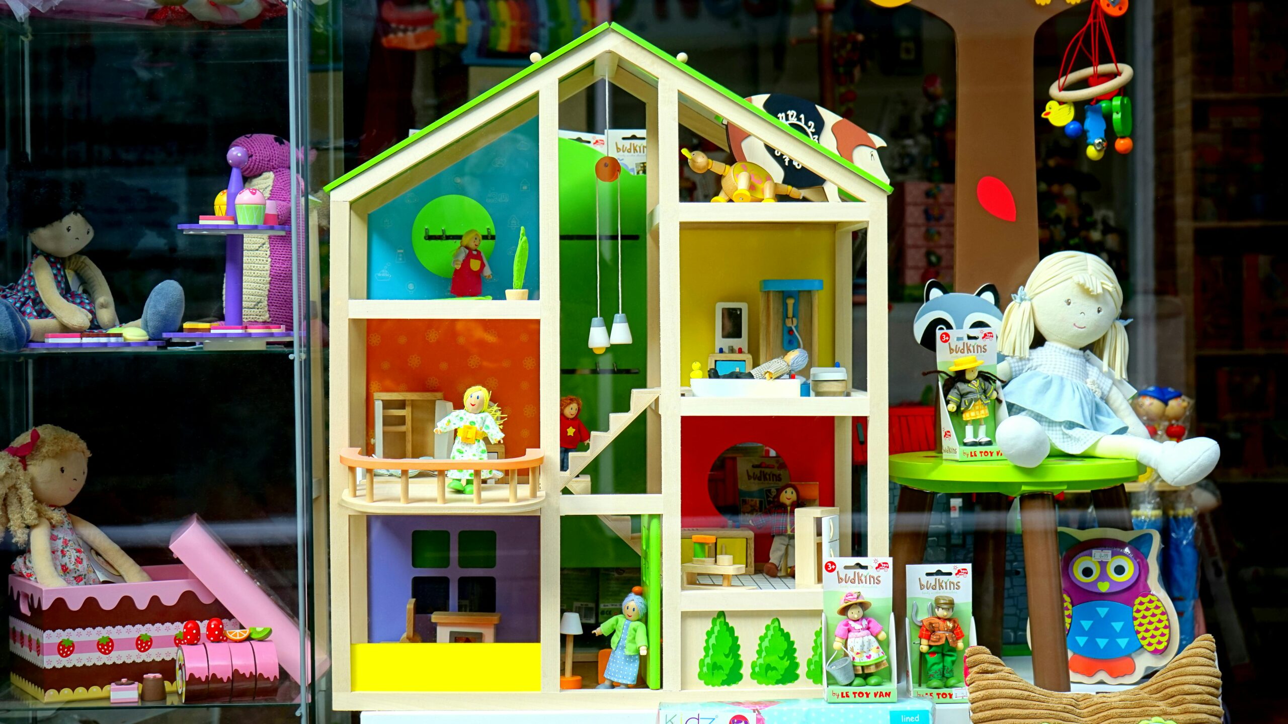 A vibrant dollhouse and stuffed toys displayed in a toy store window, perfect for children's play.